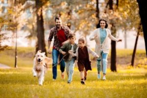 Family of four running through park with dog